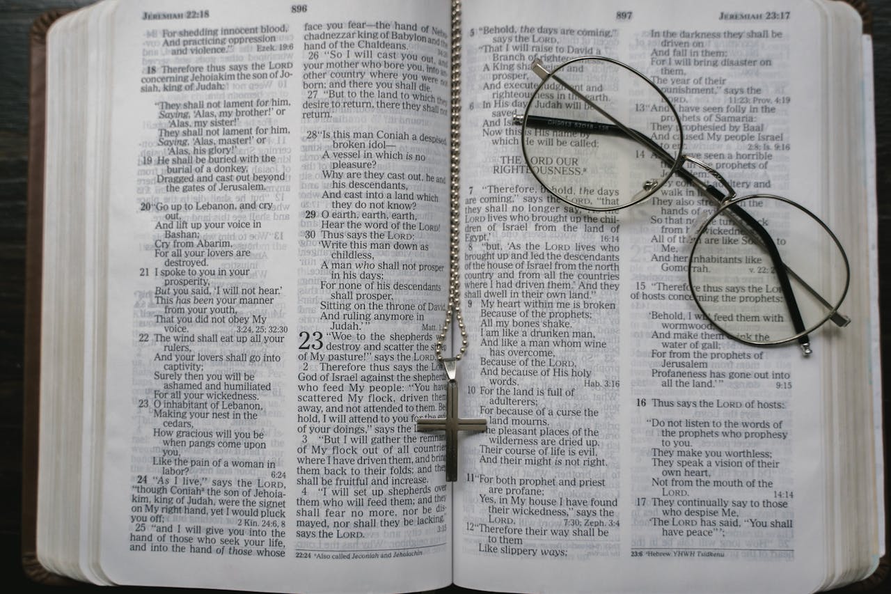 Close-up of an open Bible with a cross necklace and eyeglasses resting on the pages.