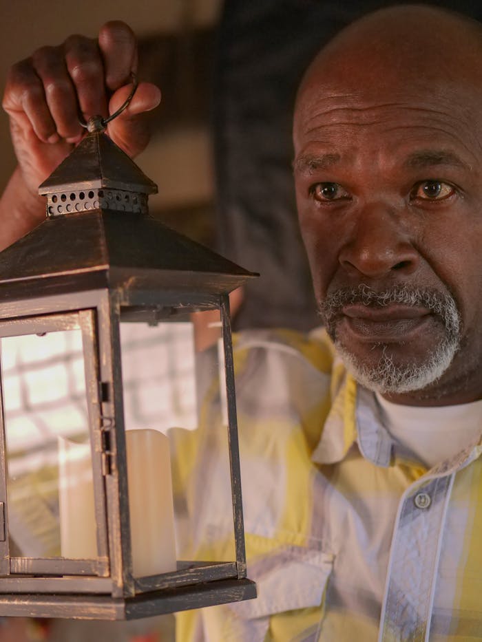 Senior man holding a lantern, evoking themes of reflection and nostalgia indoors.