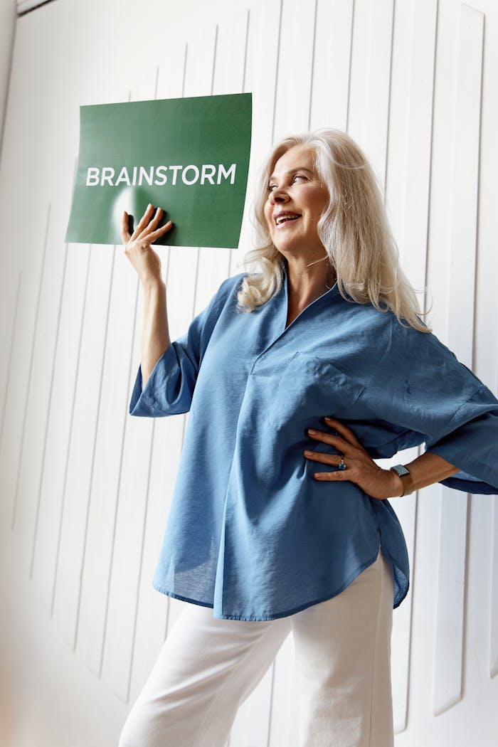 Confident senior woman posing with a 'Brainstorm' sign, highlighting creativity and wisdom.